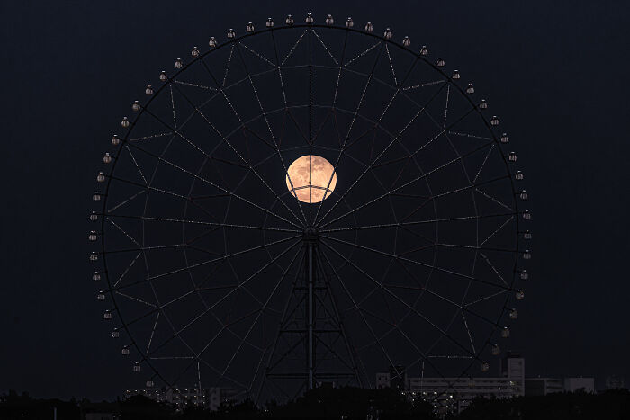 Full moon perfectly centered within the outline of a large Ferris wheel, showcasing stunning minimalism in nighttime photography.
