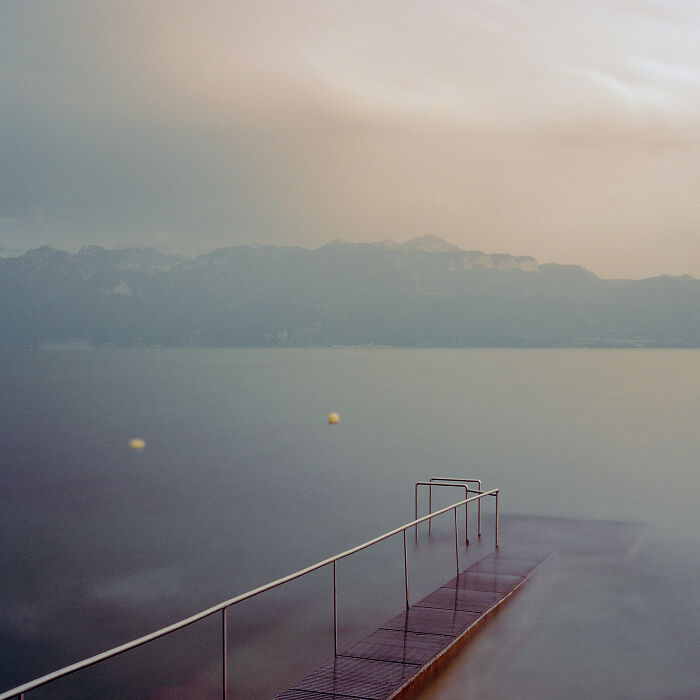 Minimalism captured in a serene lakeside scene with a simple pier extending into calm water under soft light.