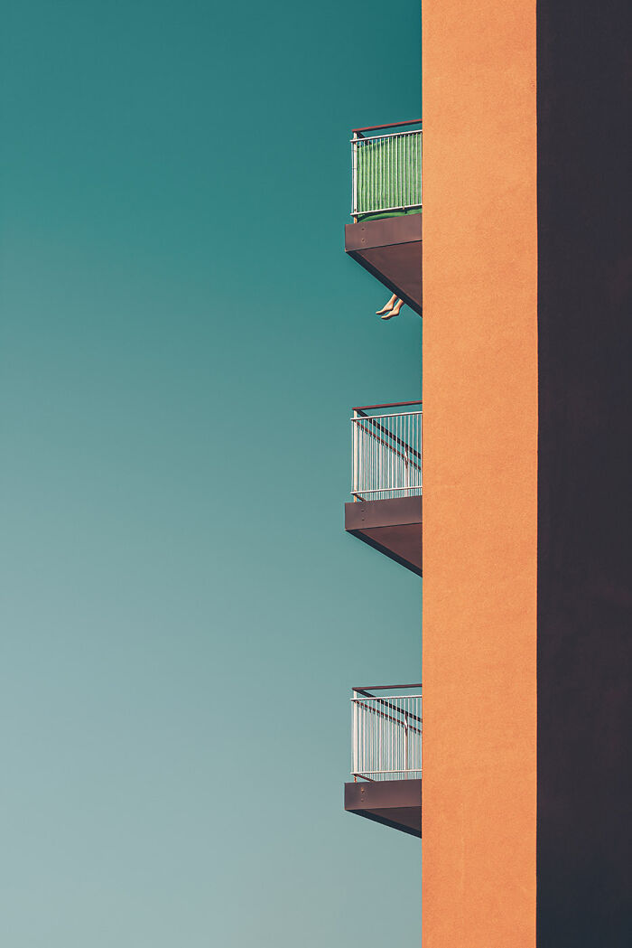Minimalism in architecture with clean lines, orange building wall and balconies against a clear blue sky.
