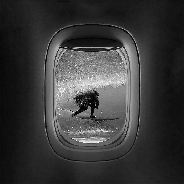 Surfer riding a wave viewed through an airplane window, showcasing stunning minimalism in black and white.