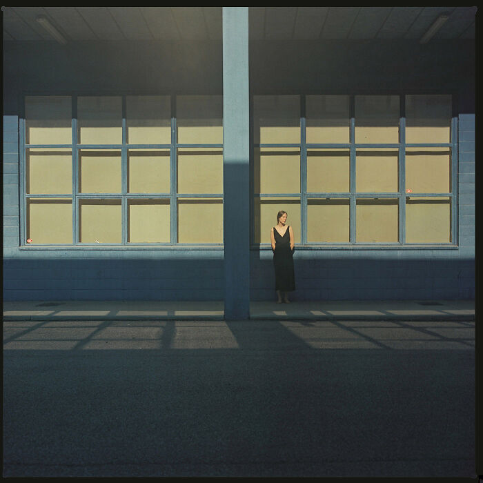 Woman in a black dress standing alone by large windows showcasing minimalism in architecture and light.