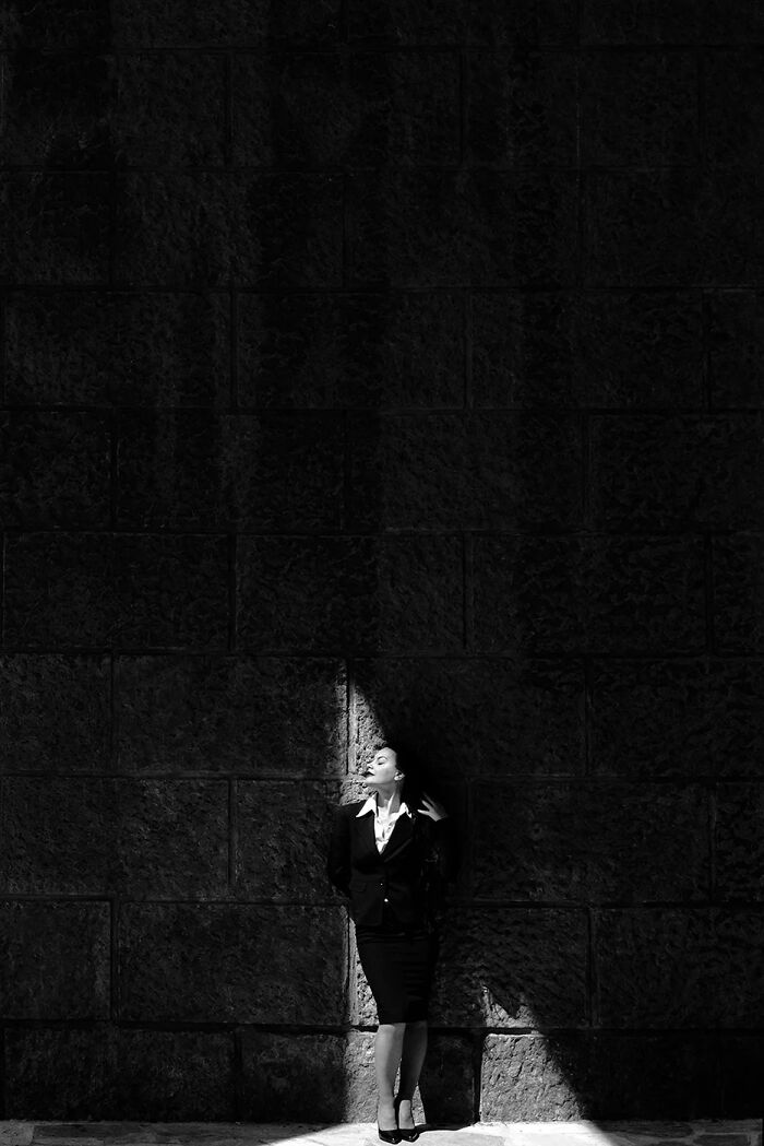 Woman in black suit standing in dramatic light against textured wall showcasing minimalism in photography.