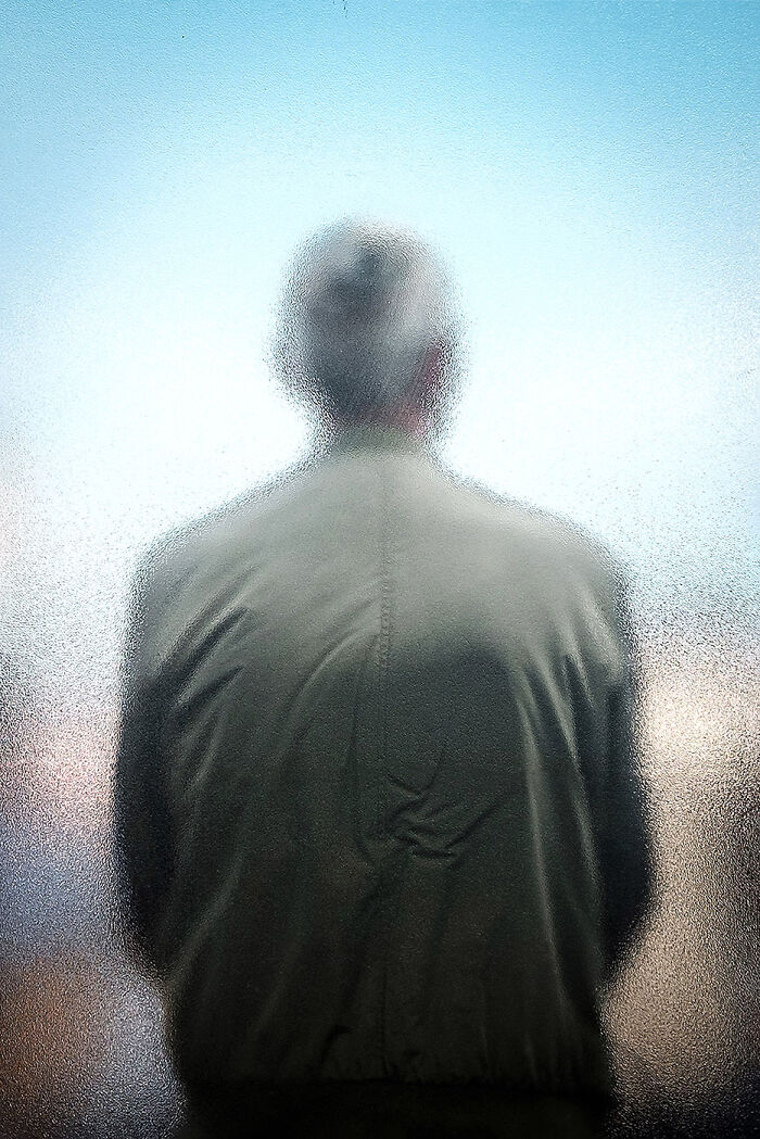 Man seen from behind through frosted glass, capturing minimalism with soft muted colors and simple composition.