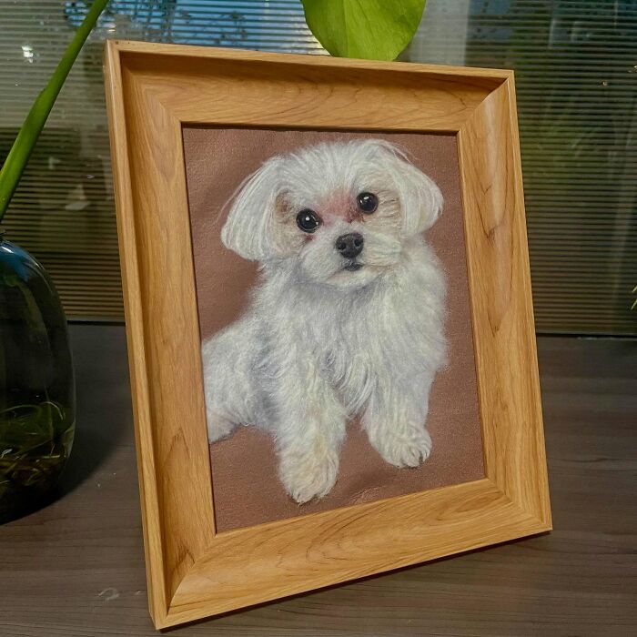 Framed wool felt pet of a white dog, showcasing realistic texture and detailed craftsmanship on a brown background.