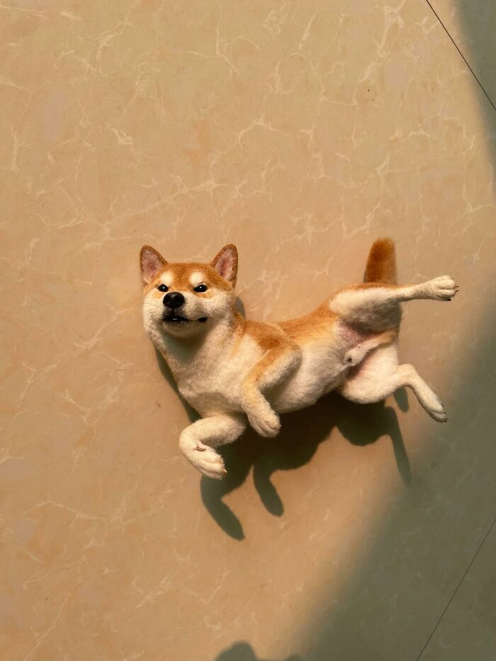 Realistic wool felt Shiba Inu pet lying on tiled floor with detailed fur and lifelike expression in natural sunlight.