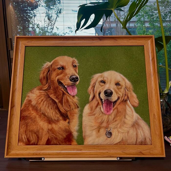 Framed wool felt pets artwork depicting two lifelike golden retriever dogs with tongues out on a green background.