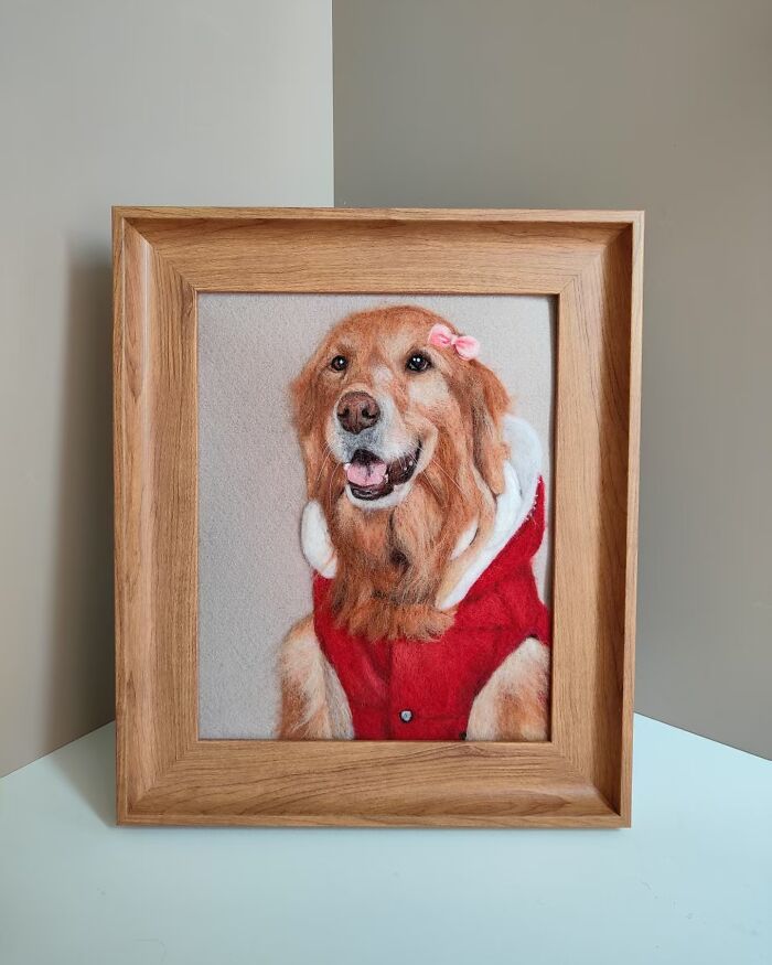 Framed wool felt pet portrait of a golden retriever wearing a red jacket and pink bow, highly realistic needle felt art.