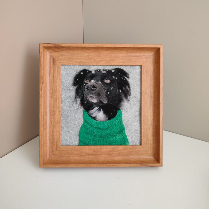 Framed wool felt pet portrait of a black dog wearing a green sweater with snowflakes on its fur.
