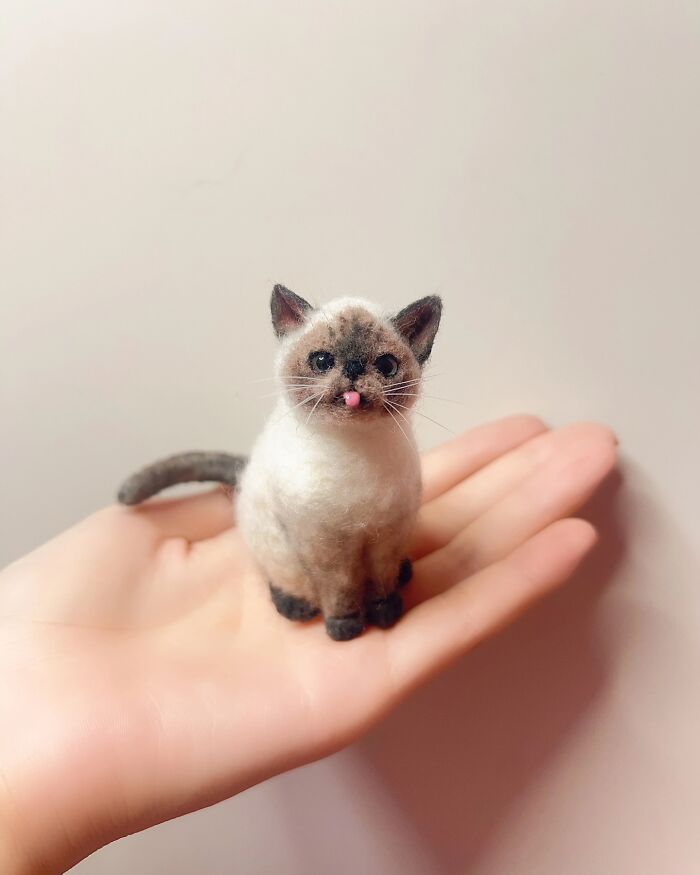Small wool felt pet cat with realistic features sitting on an open hand, showcasing detailed needle felting craftsmanship.