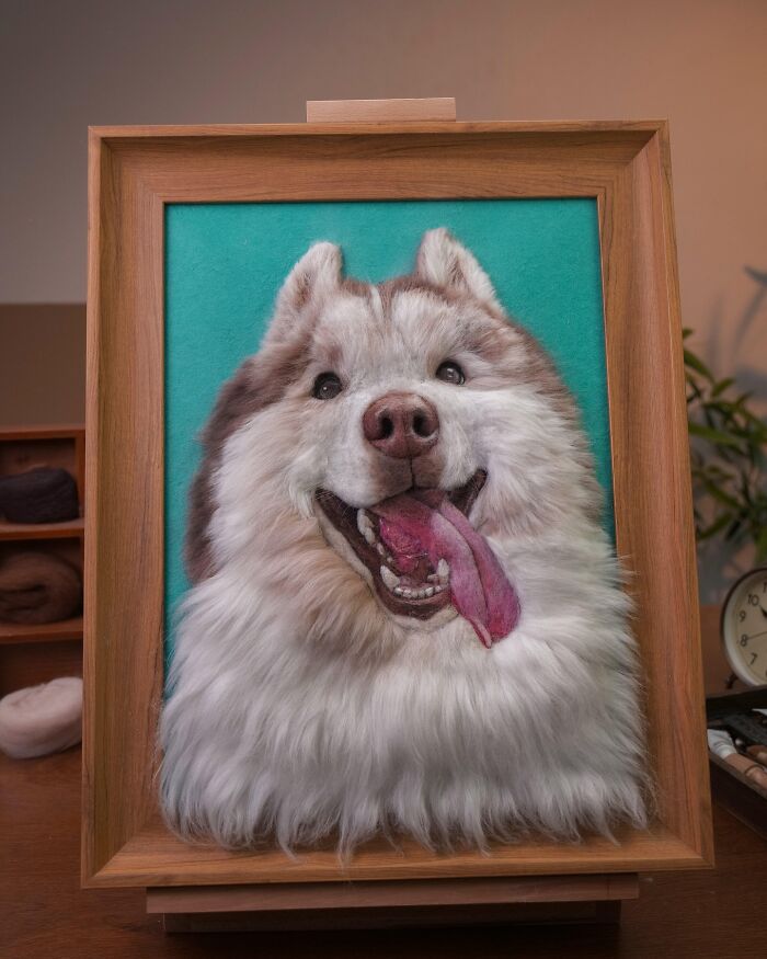 Realistic wool felt pet portrait of a happy fluffy dog with tongue out in a wooden frame on a table.