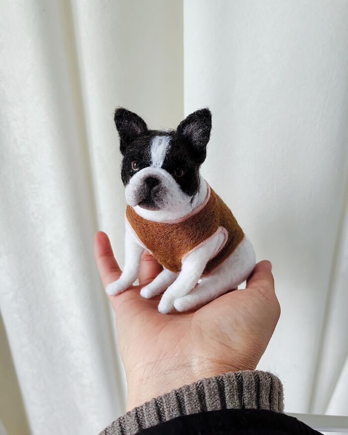 Realistic wool felt pet dog sitting on a hand, showcasing detailed needle-felted craftsmanship and lifelike texture.