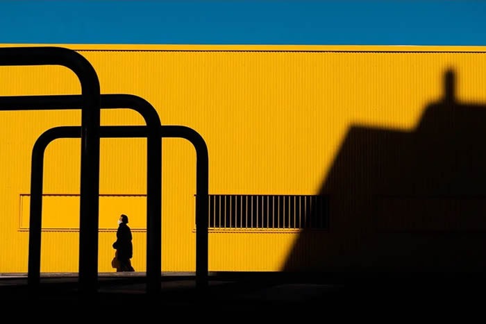Silhouette of a person walking past geometric shadows on a bright yellow wall, showcasing stunning photos from around the world.