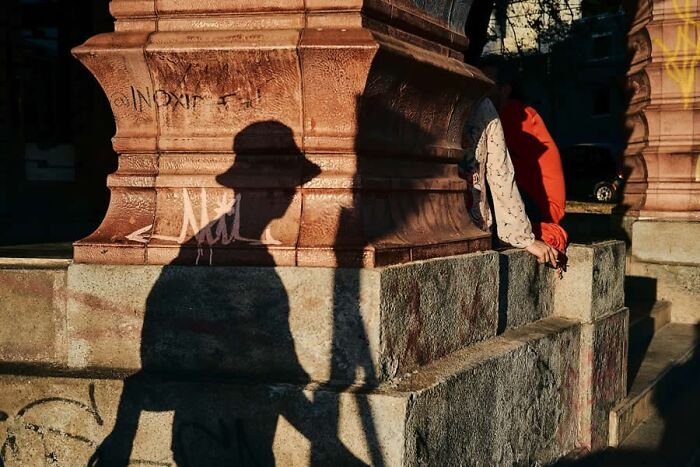 Shadowed people lean against a stone pillar, showcasing stunning photos from around the world in urban light.
