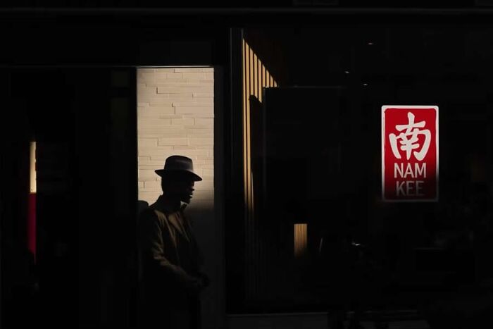 Silhouette of a man in a hat standing near a building with a Nam Kee sign in a stunning photo from around the world.