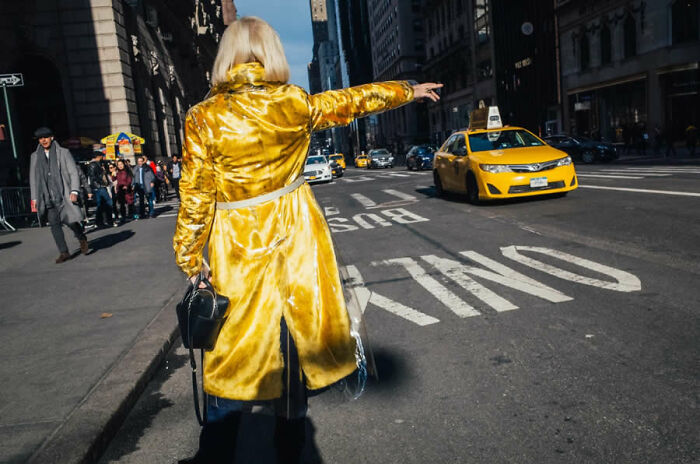 Person in a yellow coat hailing a taxi on a city street, featured in stunning photos from around the world.