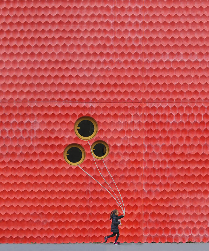 Child holding balloons in front of a textured red wall, featured in a stunning photo from around the world collection.