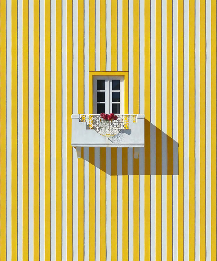 Minimalist balcony with red flowers on yellow and white striped wall, featured in stunning photos from around the world collection.