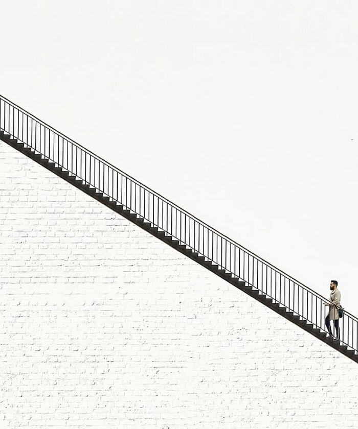 Man walking up a staircase against a white brick wall, featured in stunning photos from around the world collection.