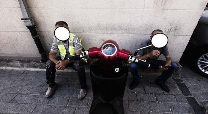 Two men sitting on a sidewalk resting beside a red scooter, showcasing stunning photos from around the world.
