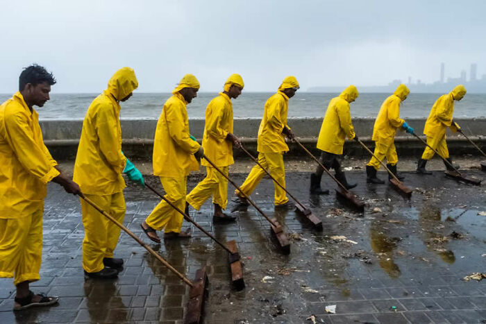 Group of workers in yellow rain gear cleaning a wet walkway, captured in a stunning photo from around the world.