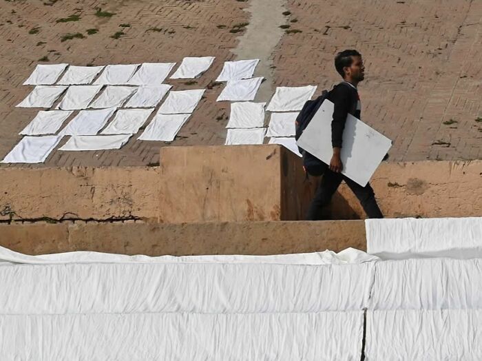 Man walking past white sheets laid out to dry on a brick surface in a stunning photo from around the world collection.