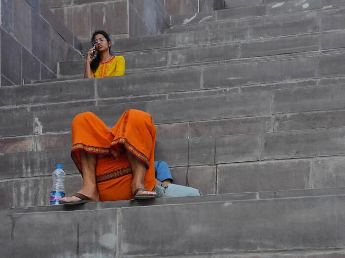 Woman in an orange outfit sitting on stairs speaking on phone, a man reclines nearby in a stunning photo from around the world.