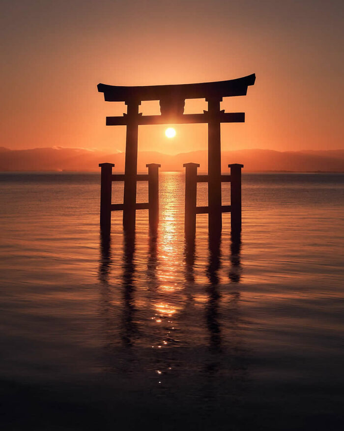 Sunset silhouette of a traditional Japanese torii gate in water, featured in stunning photos from around the world.