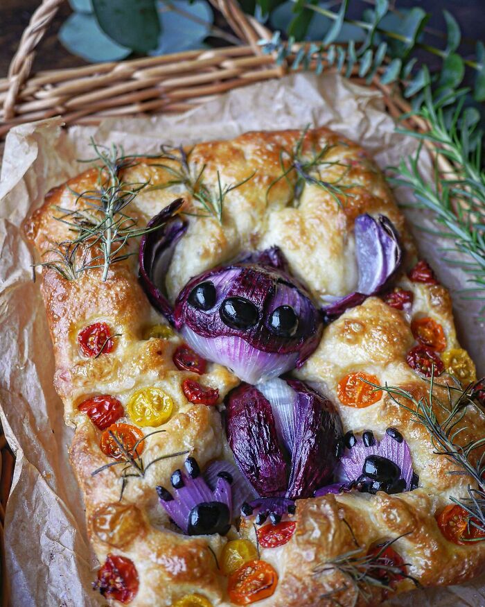Creative meal by a Japanese mom featuring a spider design with red onion, black olives, cherry tomatoes, and rosemary on bread.
