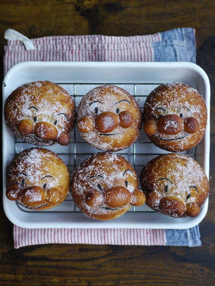 Creative meals for kids featuring six smiling, sugar-dusted bread rolls shaped like faces in a white tray.