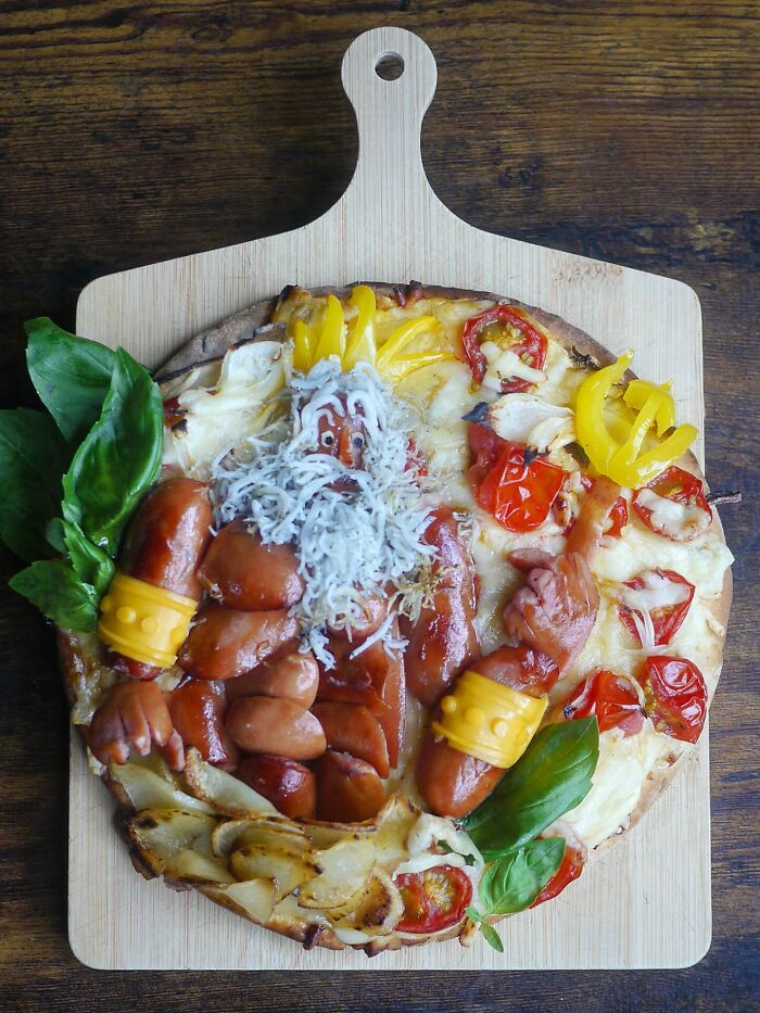 Creative meal featuring sausages, cheese, and vegetables arranged as a character on a wooden board by a Japanese mom.