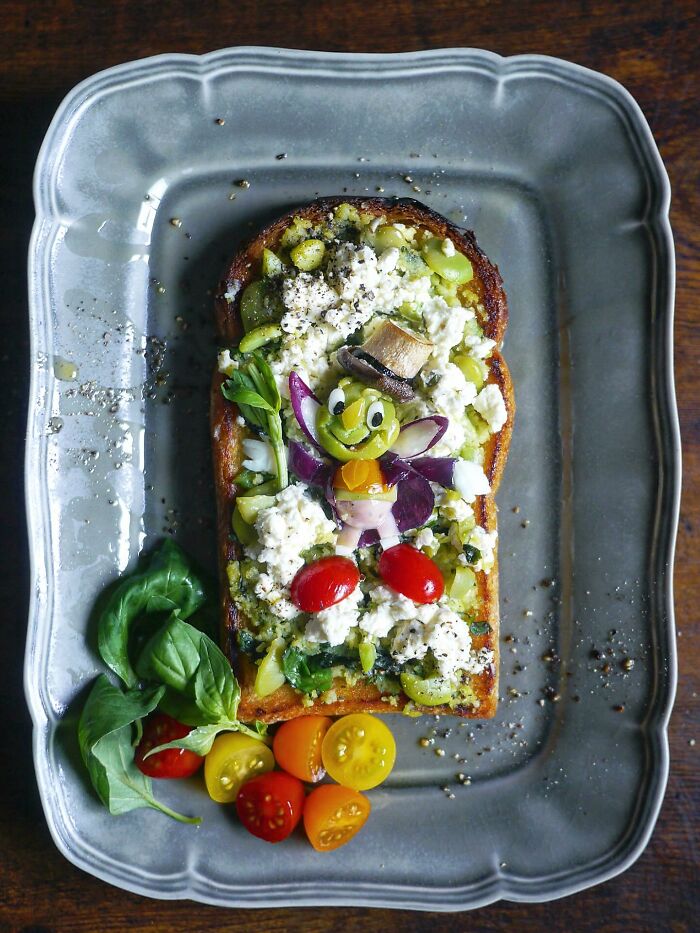Creative meal for kids featuring colorful vegetables and cheese arranged on toasted bread on a decorative gray plate.