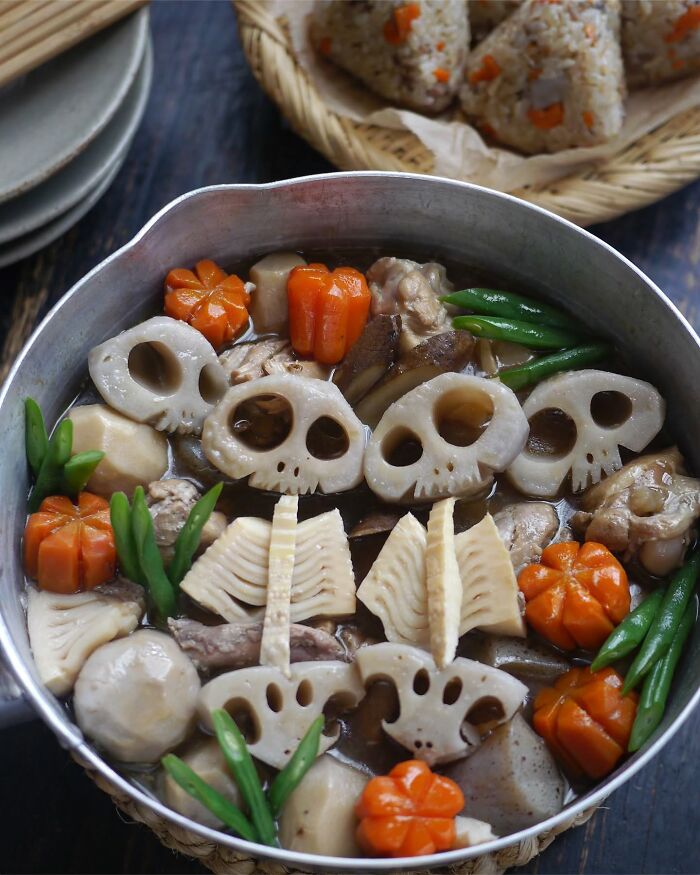 Creative Japanese mom's meal with carved lotus roots shaped like skulls and fish, surrounded by vegetables and simmered in broth.