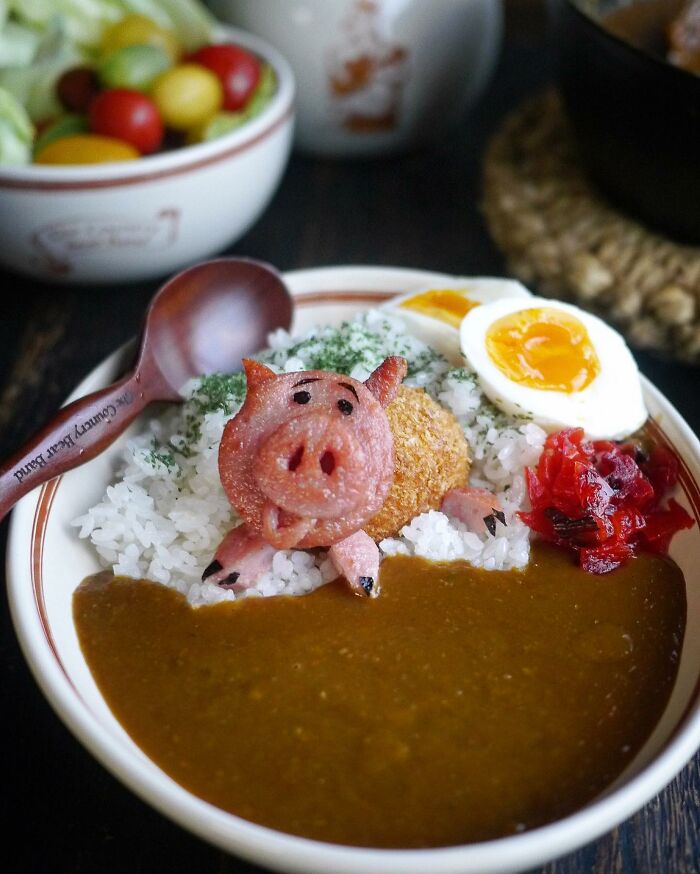 Creative Japanese kids meal featuring rice, curry, boiled eggs, and a sausage shaped like a playful pig character on the plate.