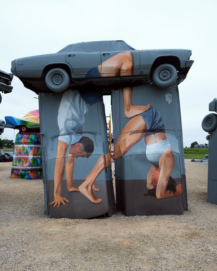 Colorful murals by Artez depicting people doing handstands painted on stacked cars in an outdoor art installation.