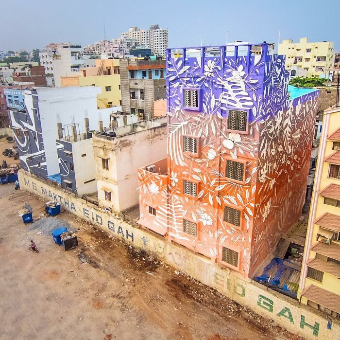 Colorful mural by Artez featuring white floral patterns on a multi-story building in an urban city setting.