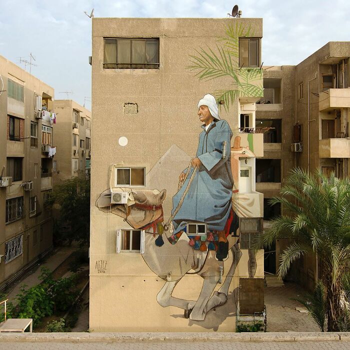 Large colorful mural by Artez depicting a man riding a camel on an urban building wall bringing city life vibrancy.