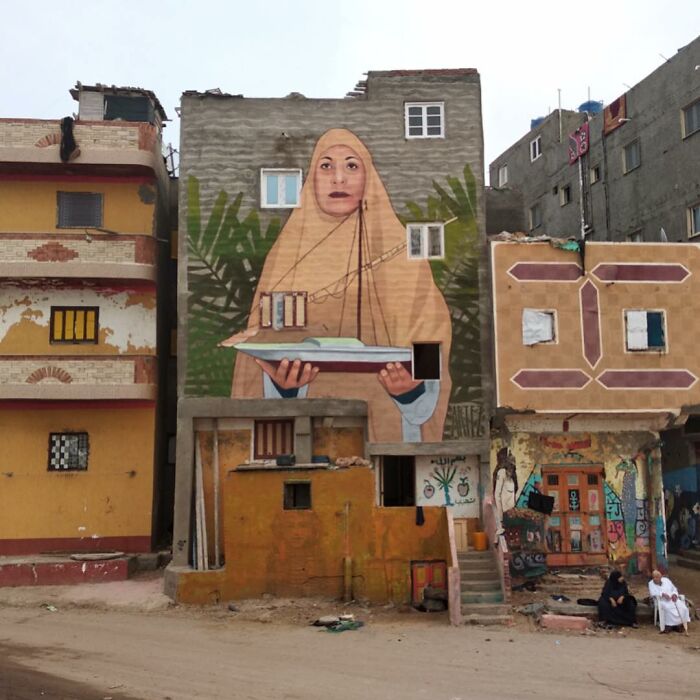 Large colorful mural of a woman holding a boat painted on the side of a city building, showcasing vibrant urban street art.
