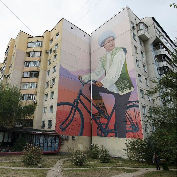 Large colorful mural by Artez of a person on a bicycle painted on the side of a city building bringing urban life.