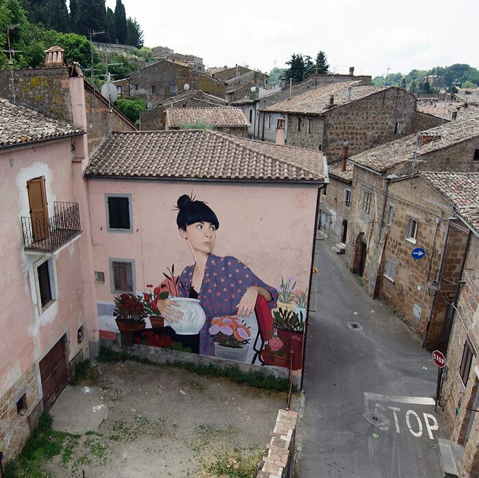 Large colorful mural by Artez depicting a woman with plants on an old building in a historic city street.