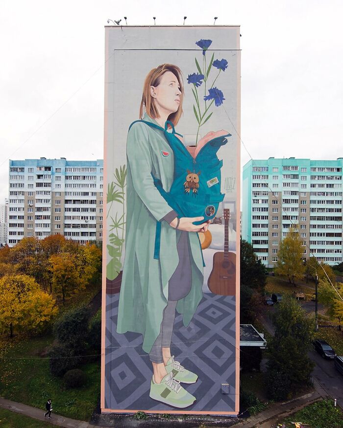 Large colorful mural by Artez on a city building showing a woman with blue flowers and urban elements.
