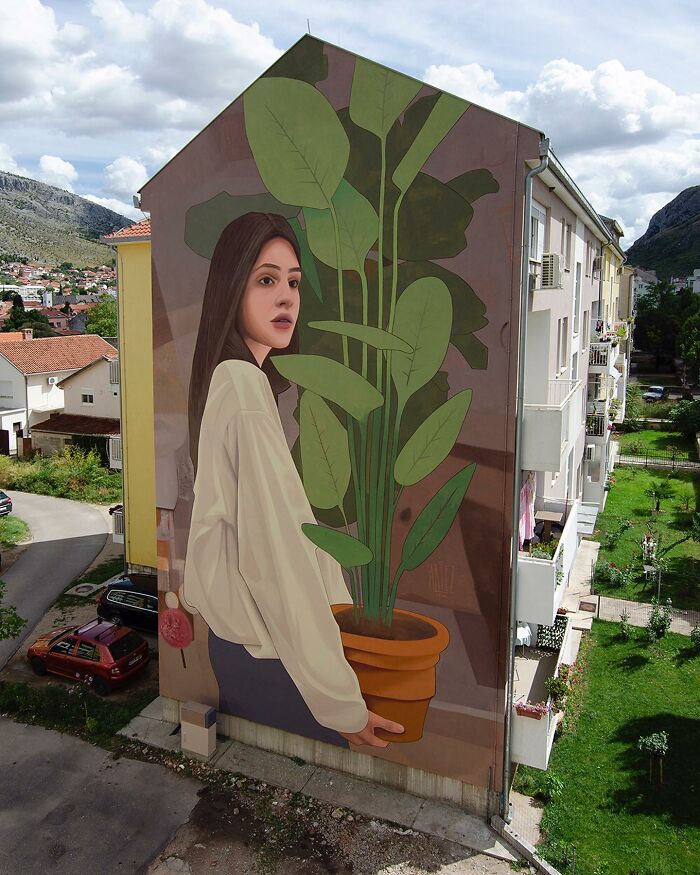 Large colorful mural by Artez of a woman holding a potted plant painted on the side of a city building.