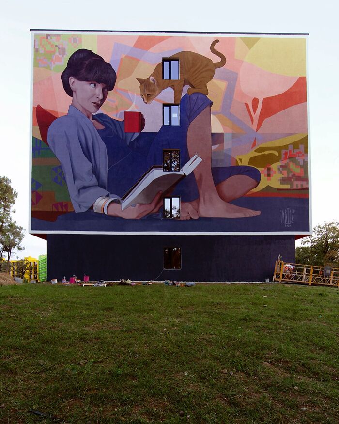 Colorful mural by Artez showing a woman reading with a cat, adding vibrant art that brings cities to life.