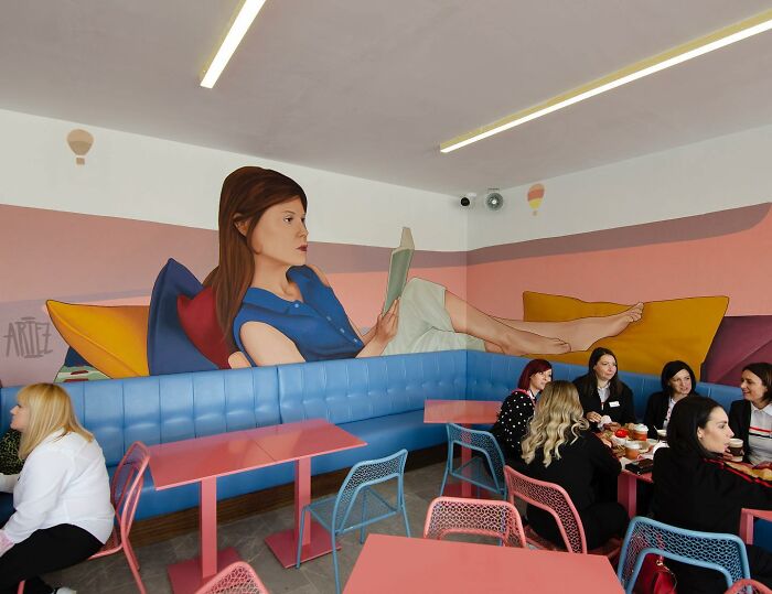 Colorful mural by Artez depicting a woman reading, brightening a cafe interior and bringing urban walls to life.