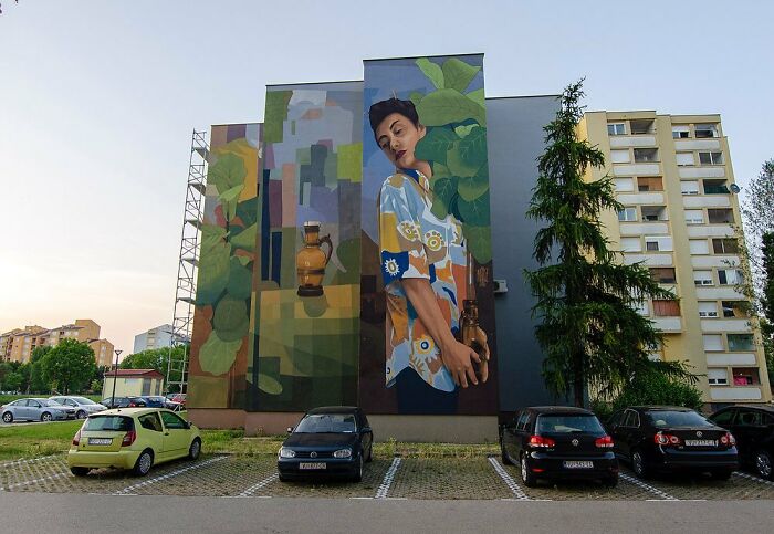 Large colorful mural by Artez on a city building wall featuring a woman holding pottery in a vibrant urban setting.