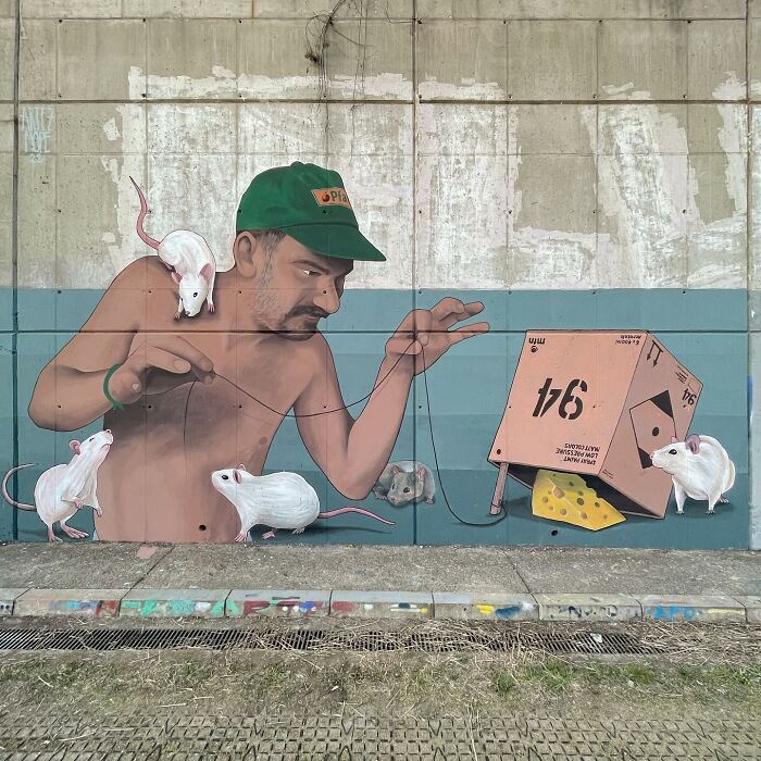 Colorful murals by Artez showing a man interacting with white mice and a cardboard mouse trap in an urban setting.