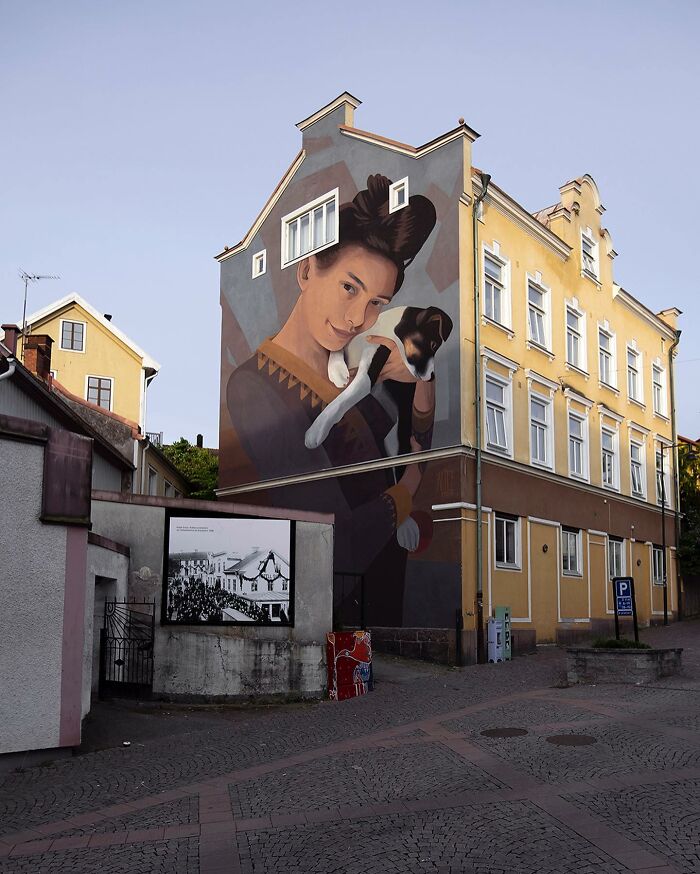 Large colorful mural by Artez on a city building wall depicting a woman holding a dog in an urban setting.