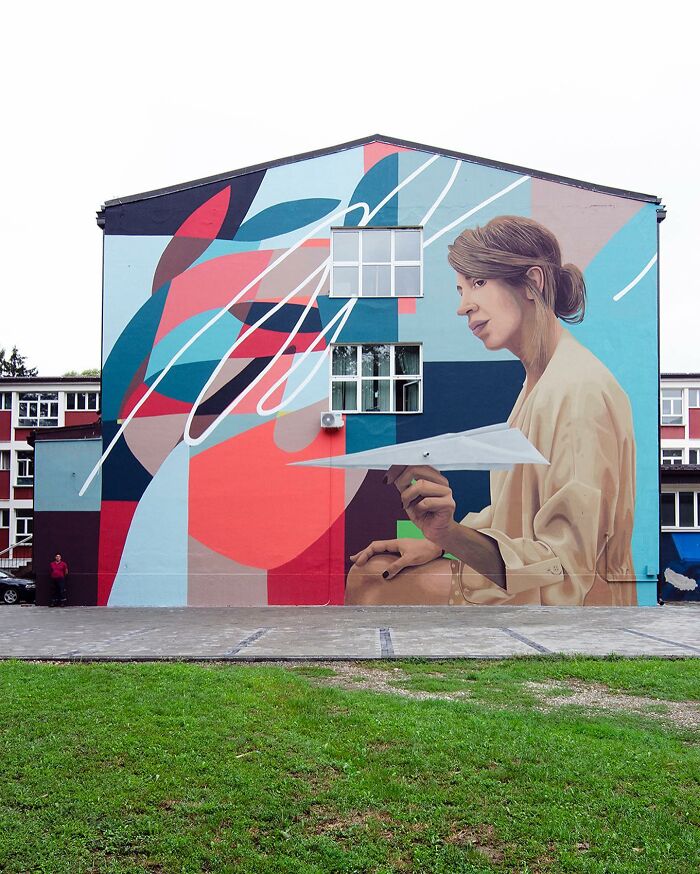 Colorful mural by Artez depicting a woman holding a paper airplane on the side of a city building.