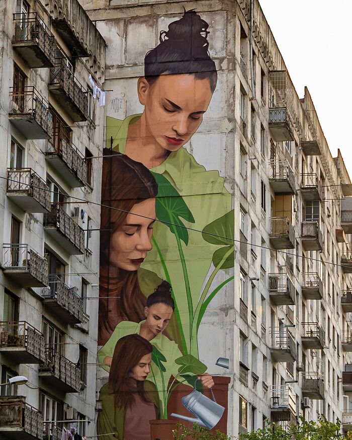 Large colorful mural by Artez on building wall featuring multiple women and green plants in an urban city setting.