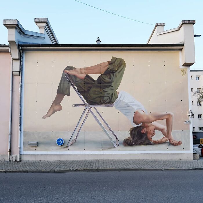 Large colorful mural by Artez depicting a person reclining backward on a chair, brightening urban city life.
