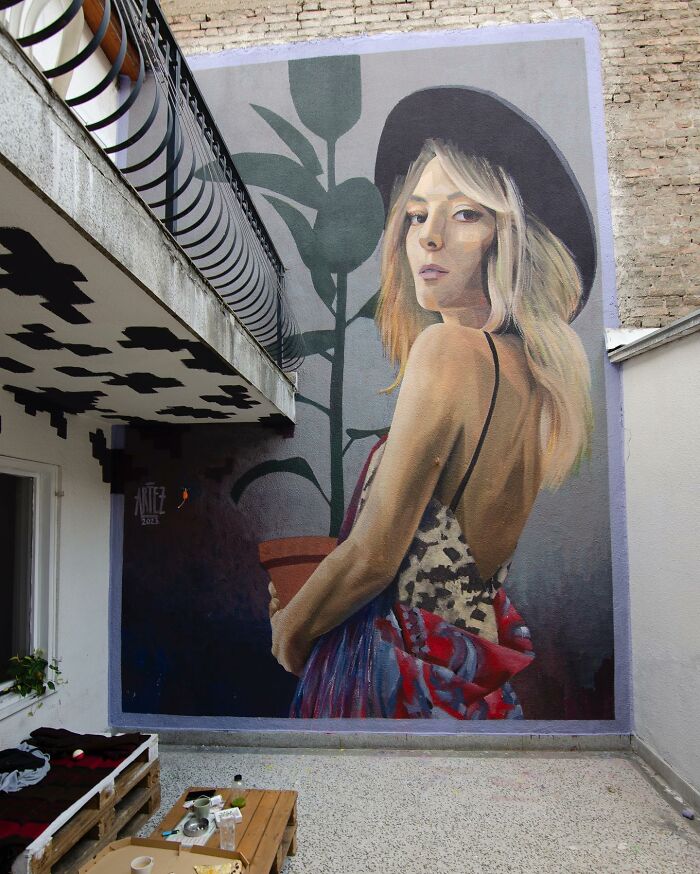 Colorful mural by Artez depicting a woman in a hat holding a potted plant, brightening an urban city space.